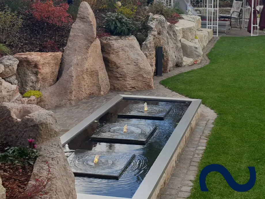 Steinplatten als Gartenbrunnen in einem großen GFK-Wasserbecken mit Edelstahlumrandung.